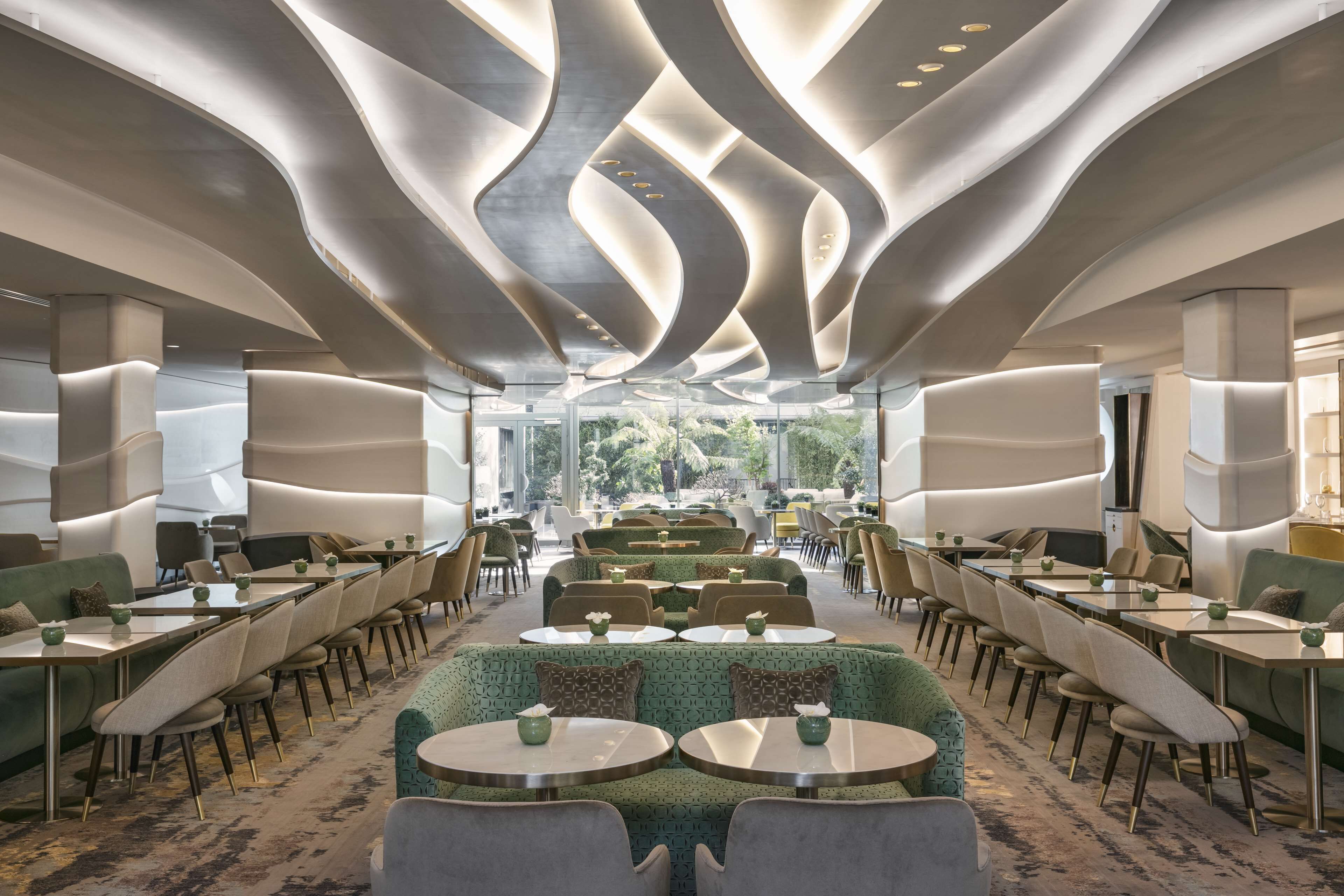 Un espace de restauration moderne doté d’un plafond au design original, de sièges verts et offrant une vue sur l’extérieur.