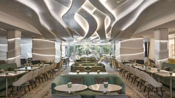 Un espace de restauration moderne doté d’un plafond au design original, de sièges verts et offrant une vue sur l’extérieur.
