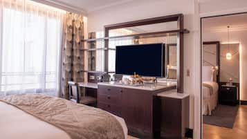 A hotel room with a bed, a desk with a flat-screen TV, a mirror, and a nightstand.