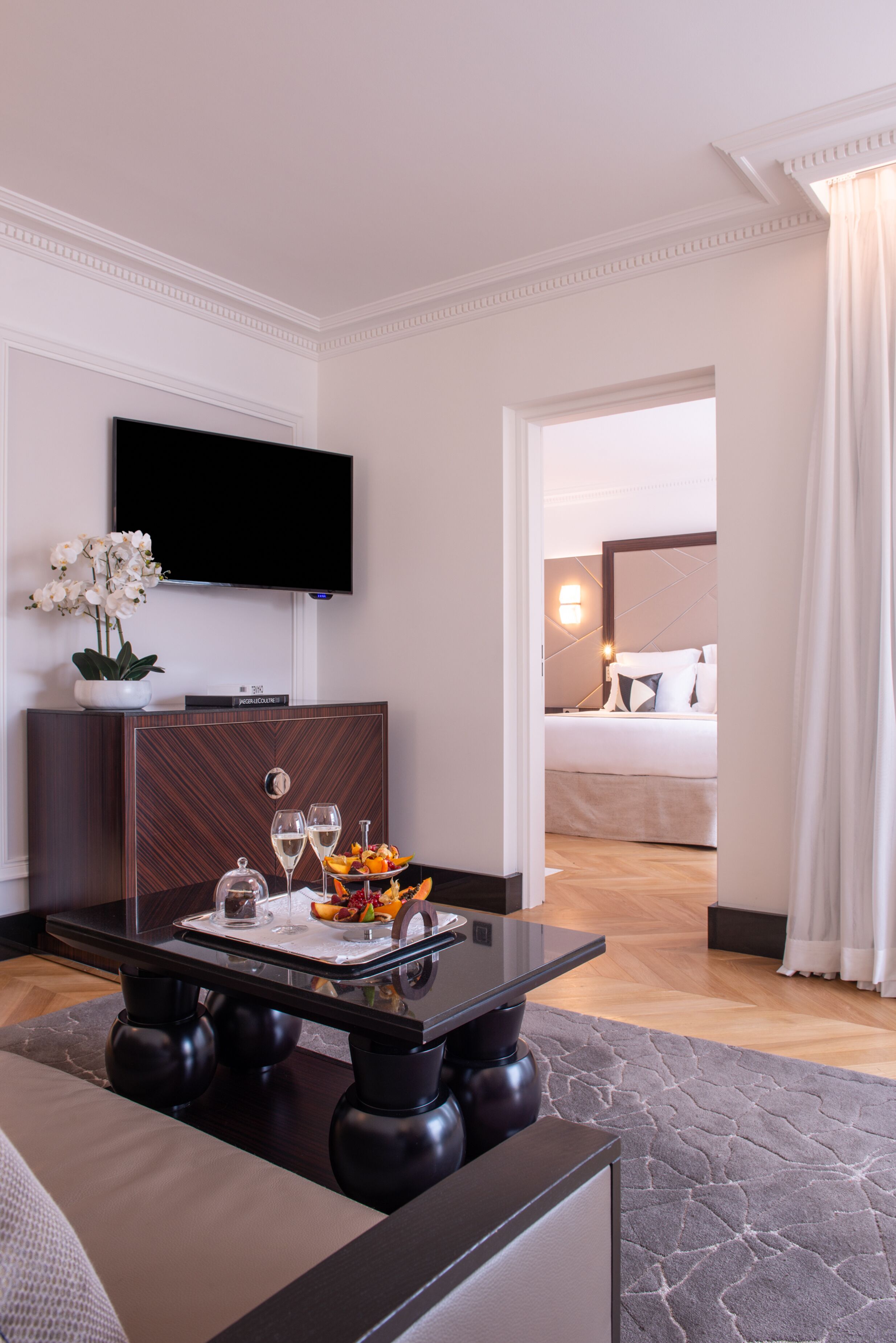 Habitación de hotel de diseño moderno, con una televisión de pantalla plana montada en la pared, una zona de comedor con mesa de vidrio y una cama con cabecero.