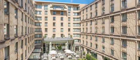 A multi-story hotel with a central courtyard featuring outdoor seating and a glass-roofed entrance.