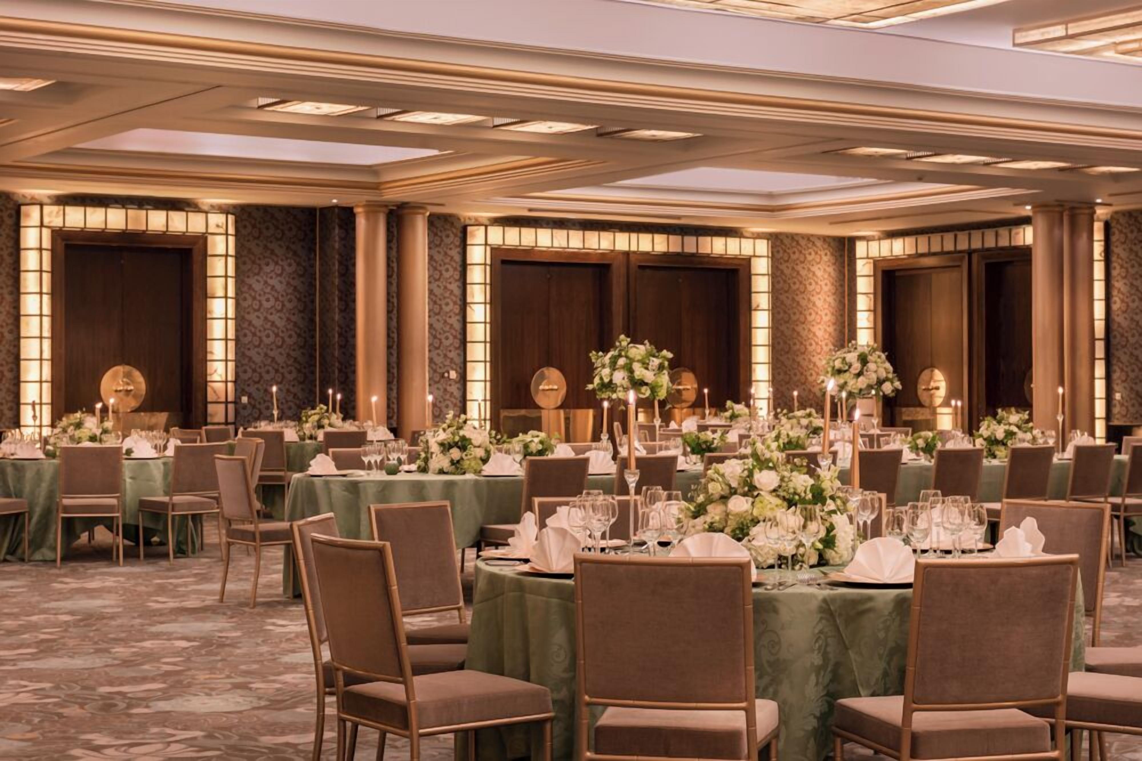 A banquet hall with round tables set for dining, each with a green tablecloth and white centerpieces.