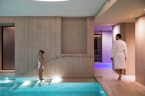 Un espace piscine intérieur moderne, avec un plancher en bois, une rambarde en verre et une personne portant un maillot de bain.