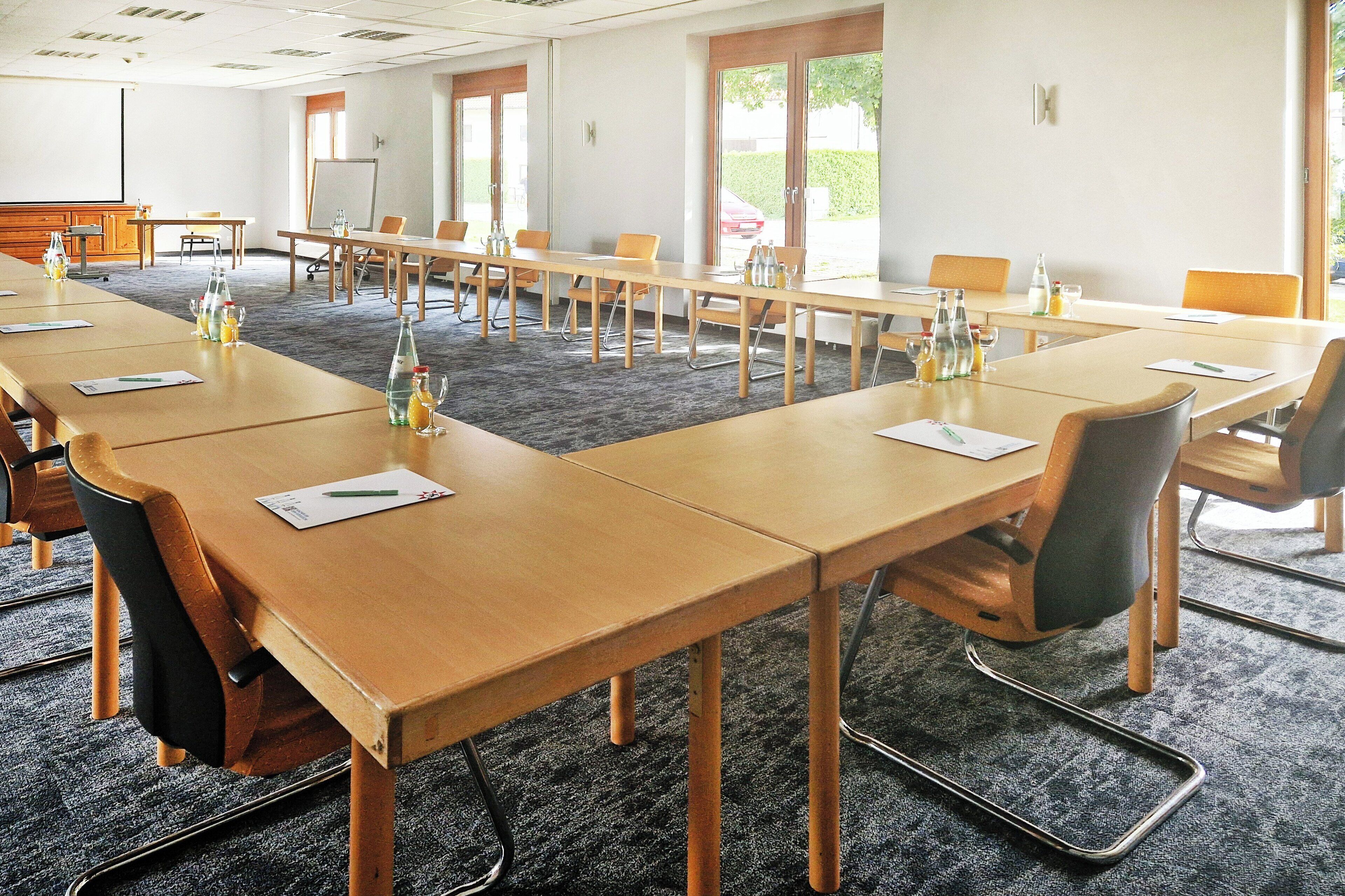 Konferenssitila, jossa on pitkiä pöytiä, tuoleja ja projektorikangas.