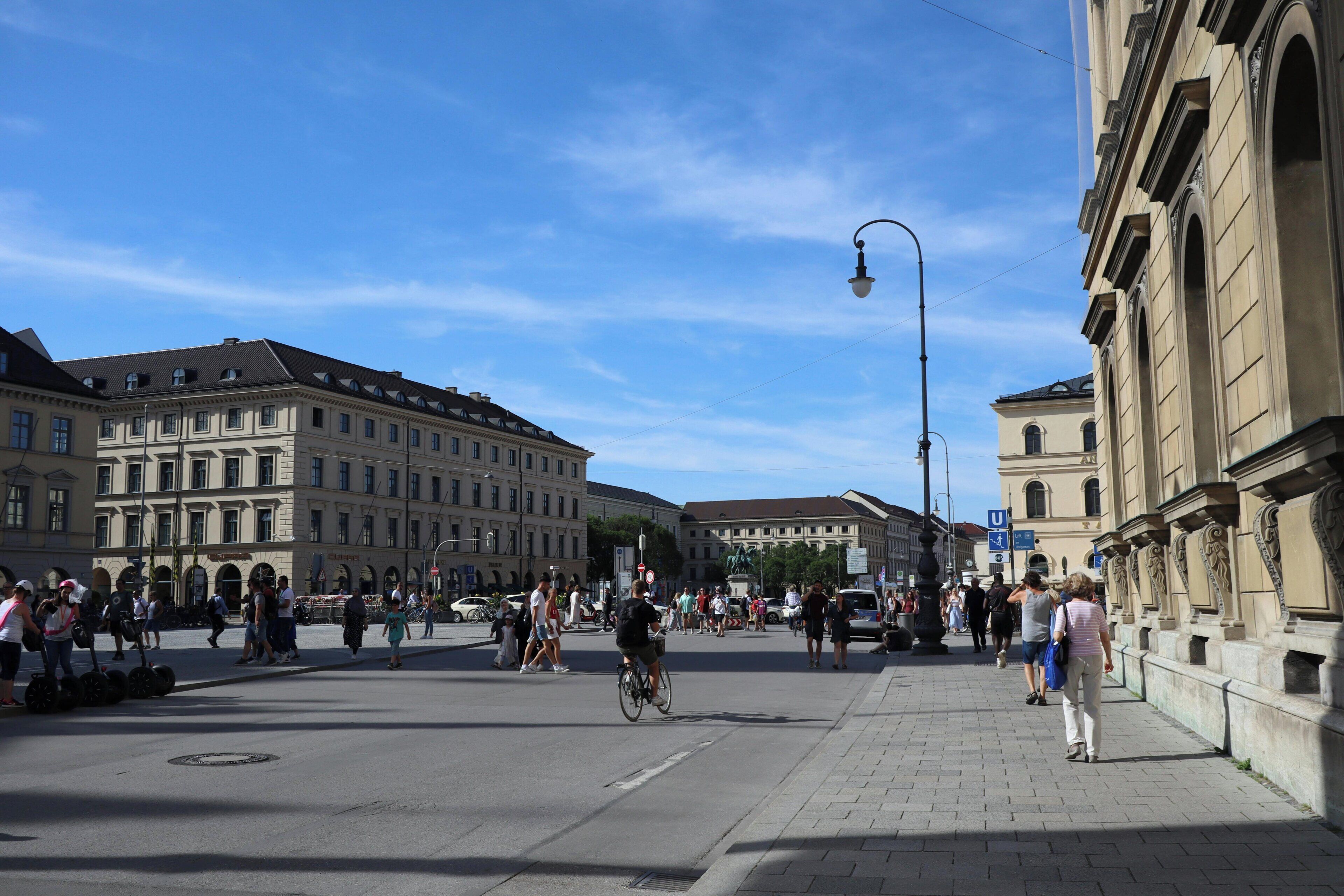 Une place publique où l’on peut voir des piétons, un cycliste et des bâtiments historiques.