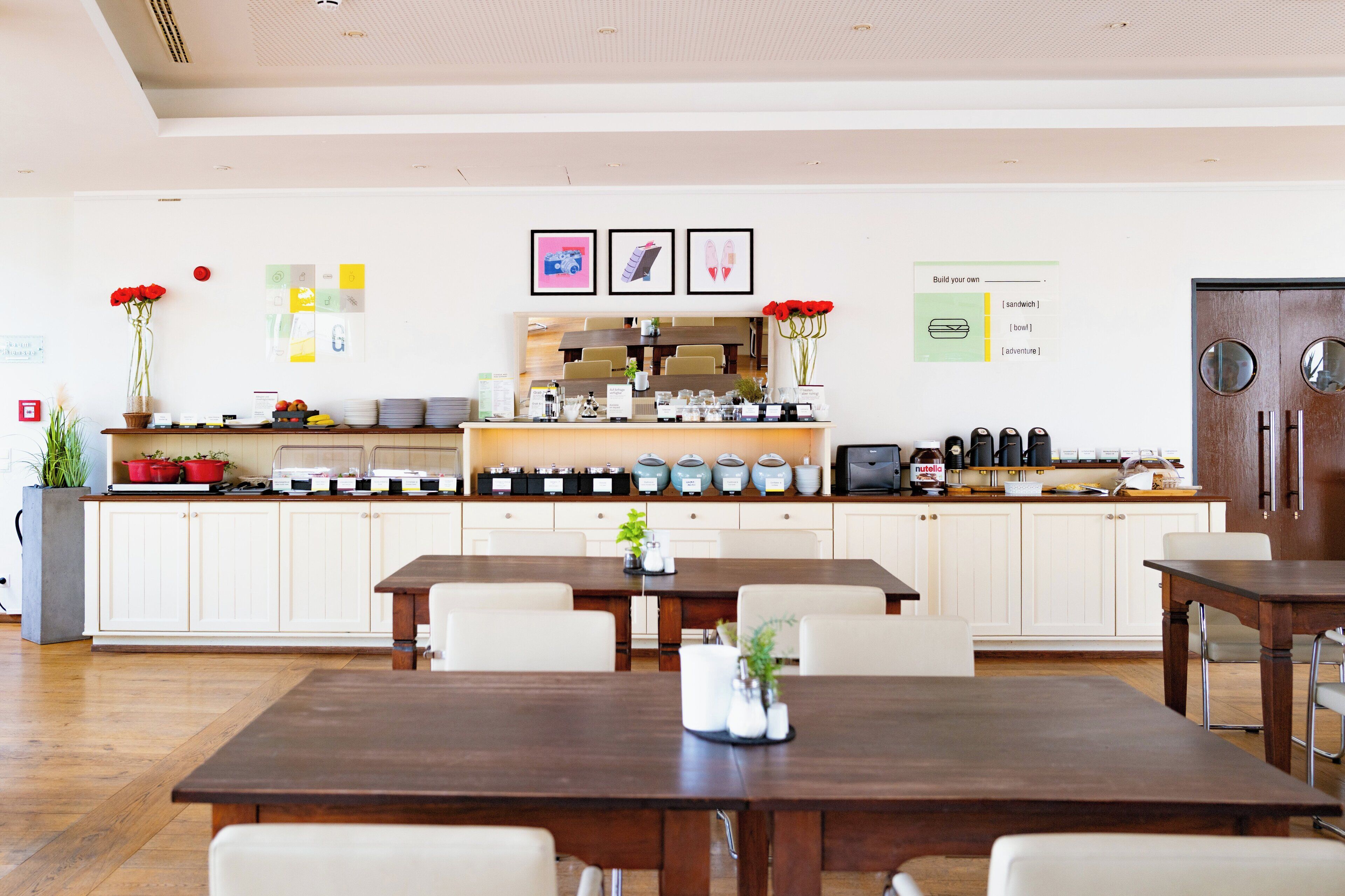 A modern dining area with a long wooden table, white cabinets, and a kitchen counter with various items.