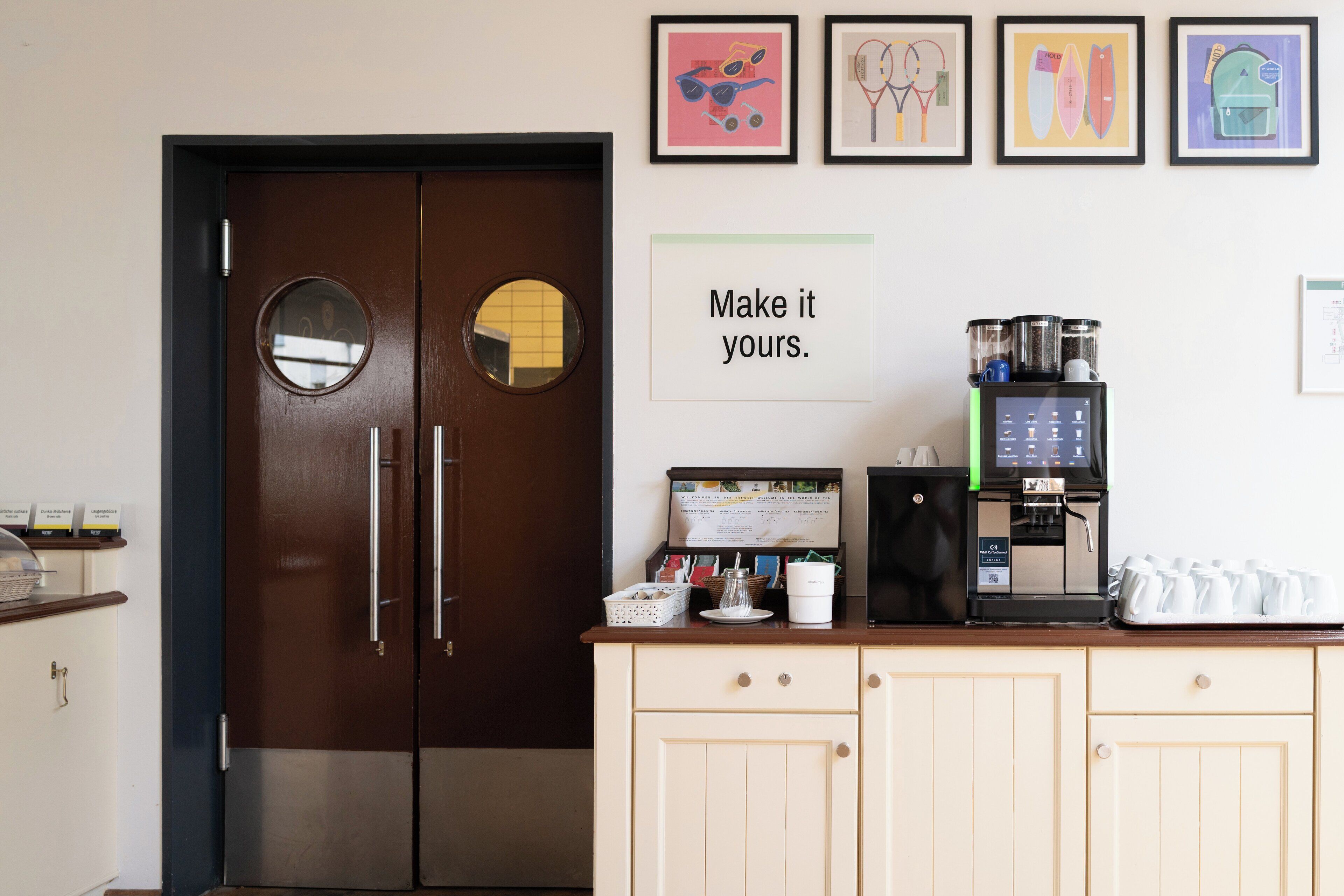 A coffee station with a coffee machine and cups, a sign that says 'Make it yours.', and a door with a round mirror.