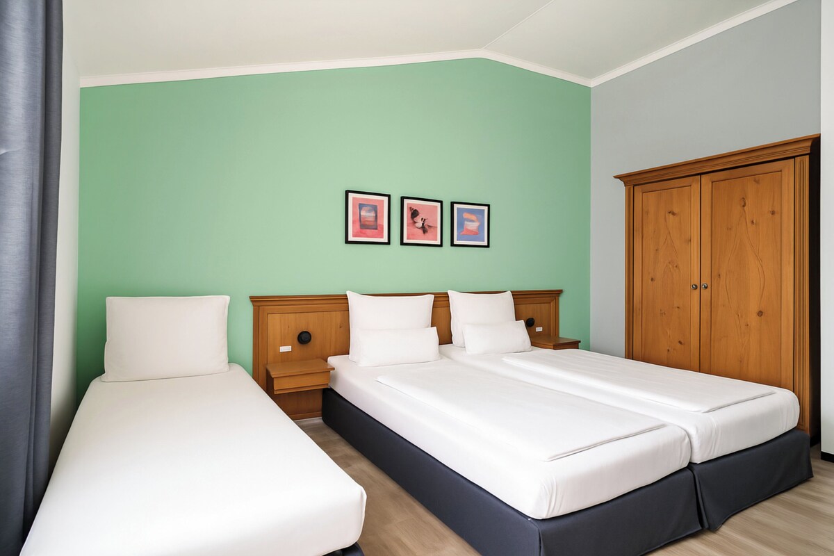 A double room with two beds, a wardrobe, and three framed pictures on the wall.