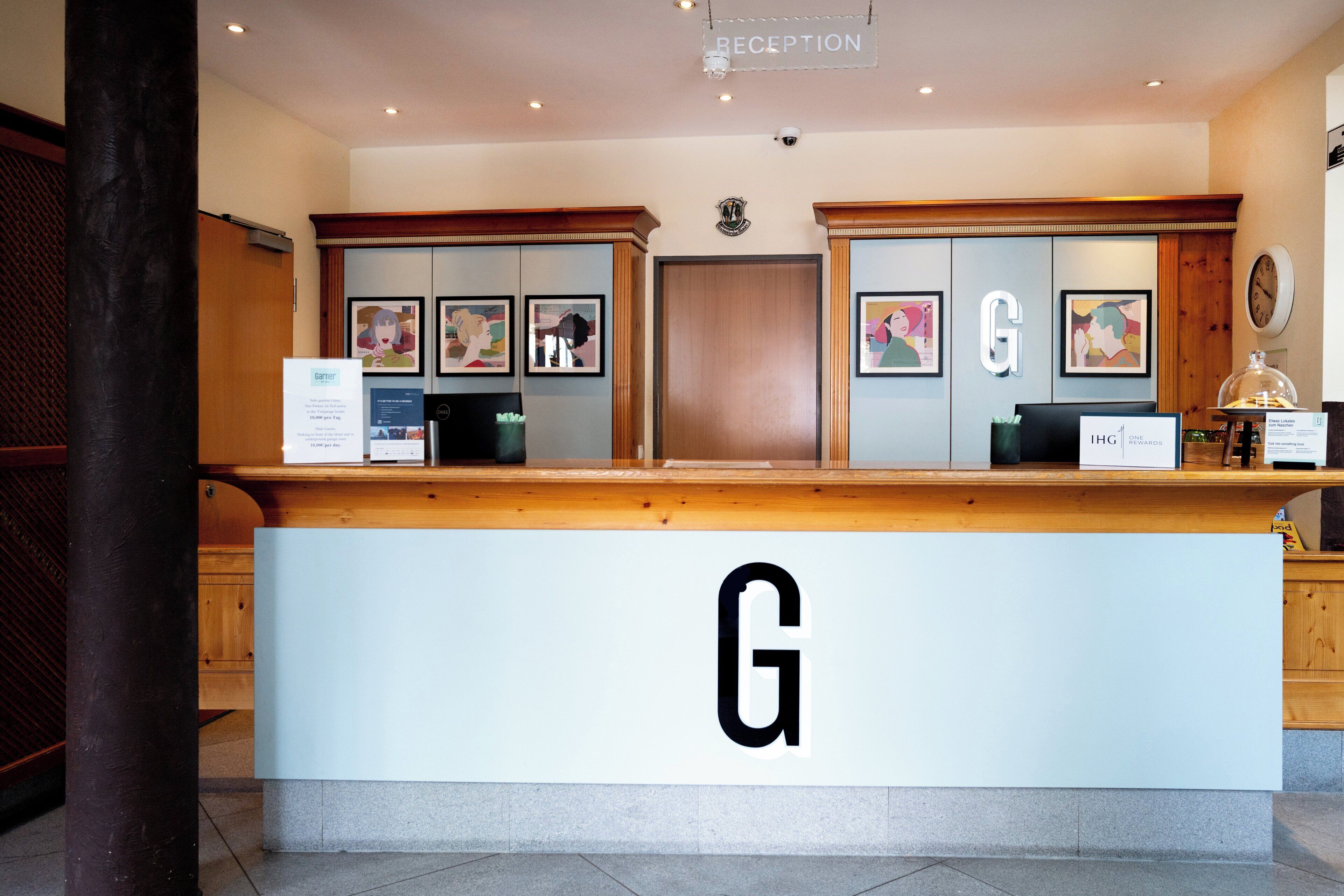 A reception desk with a large 'G' sign, framed artwork on the walls, and a clock.