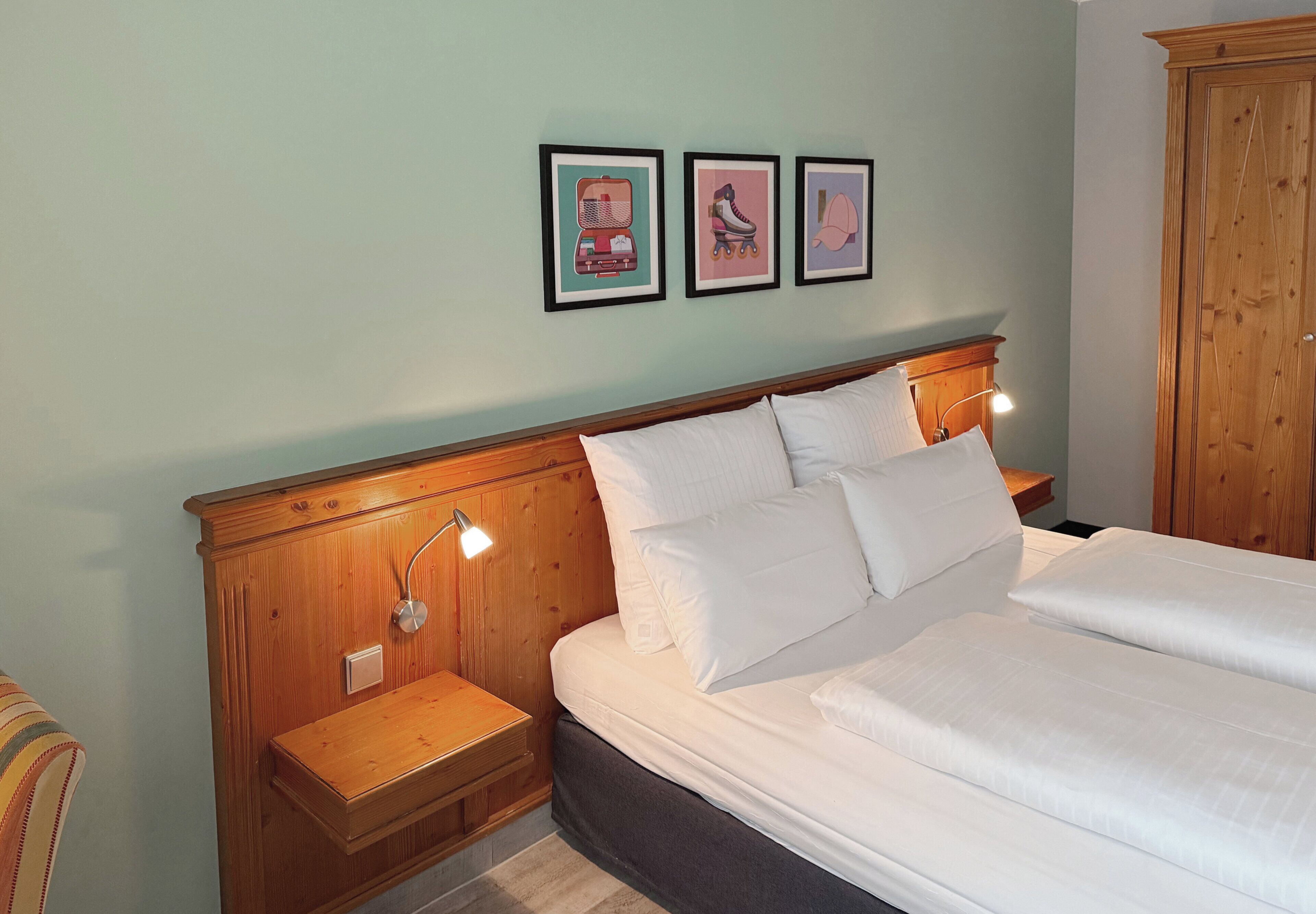 A bedroom with a wooden headboard, a bed with white linens, two bedside tables with lamps, and three framed pictures on the wall.