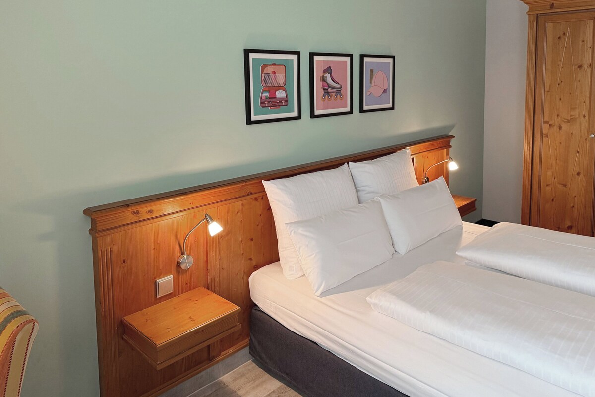 A bedroom with a wooden headboard, a bed with white linens, two bedside tables with lamps, and three framed pictures on the wall.