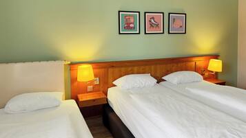 A hotel room with two single beds, wooden headboards, and a wooden nightstand with a lamp.