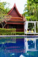 Un edificio rojo con techo triangular, una piscina y una marquesina blanca con cojines amarillos.