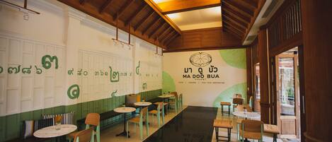 Interior de restaurante con vigas de madera, decoración verde y blanca, y mesas y sillas dispuestas para comer.