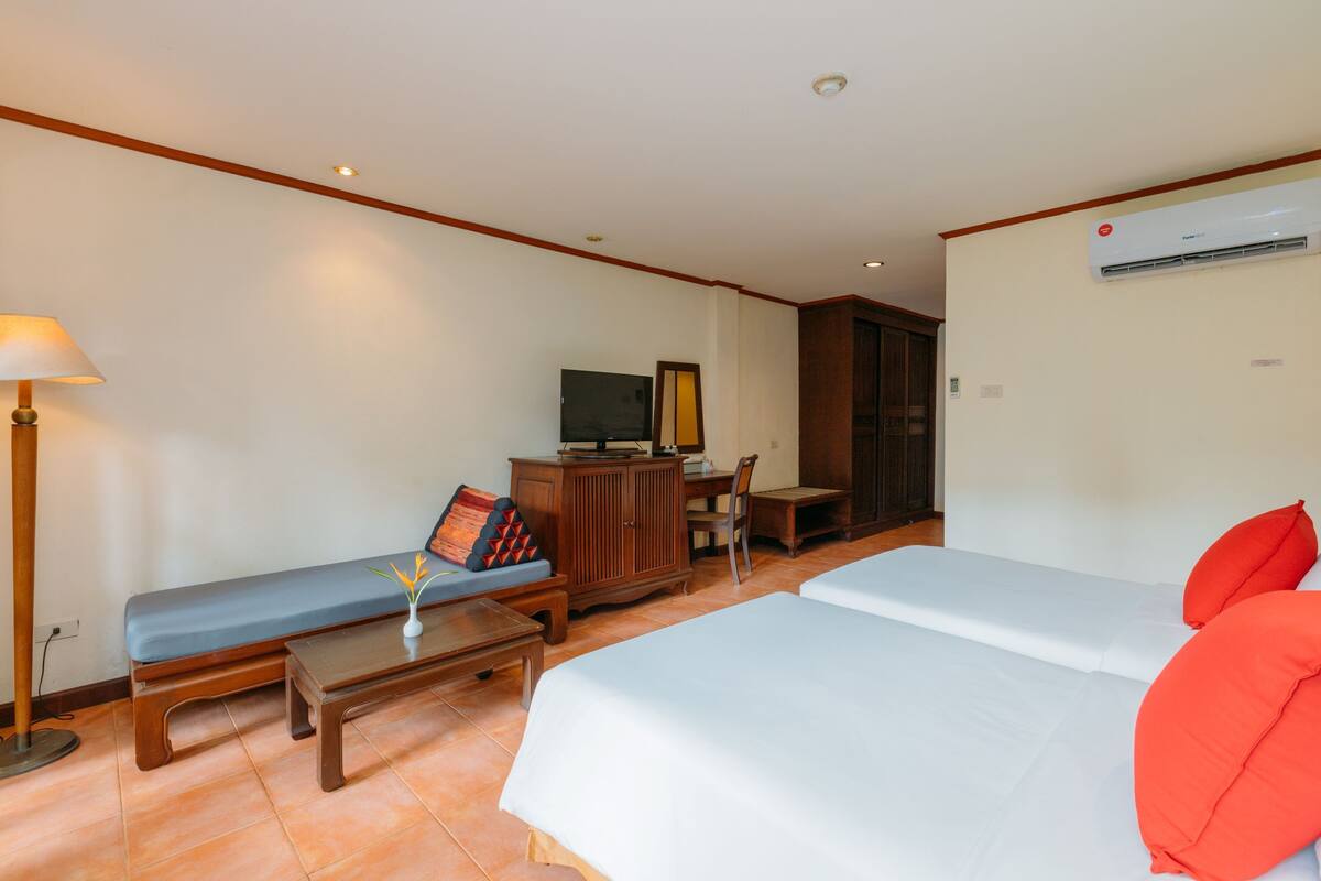 A hotel room with two beds, a desk, a television, and an air conditioning unit.