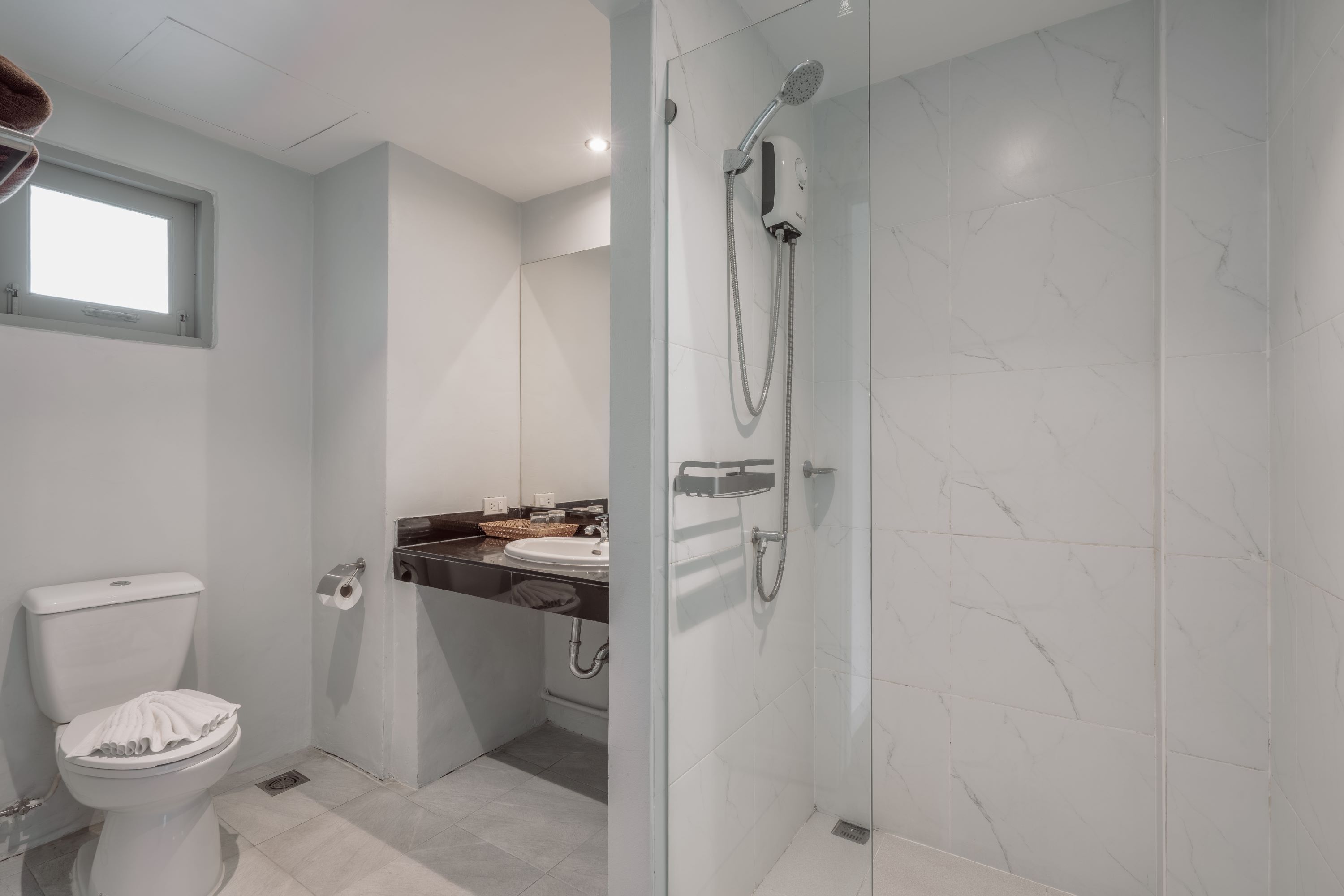 Un baño moderno con inodoro, lavamanos y ducha con mampara de vidrio.