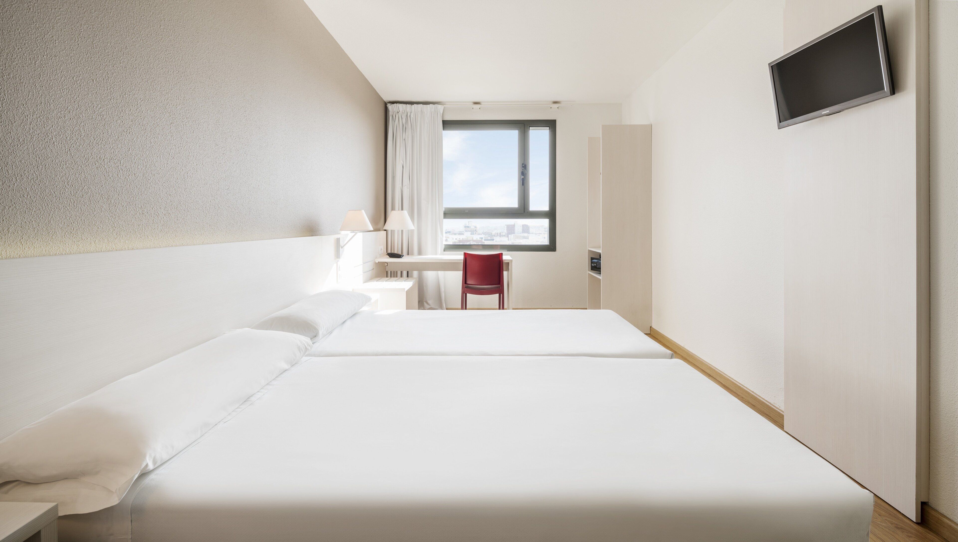 Hotellihuone, jossa on suuri sänky, työpöytä tuolilla, seinälle asennettu televisio ja ikkuna, jossa on verhot.