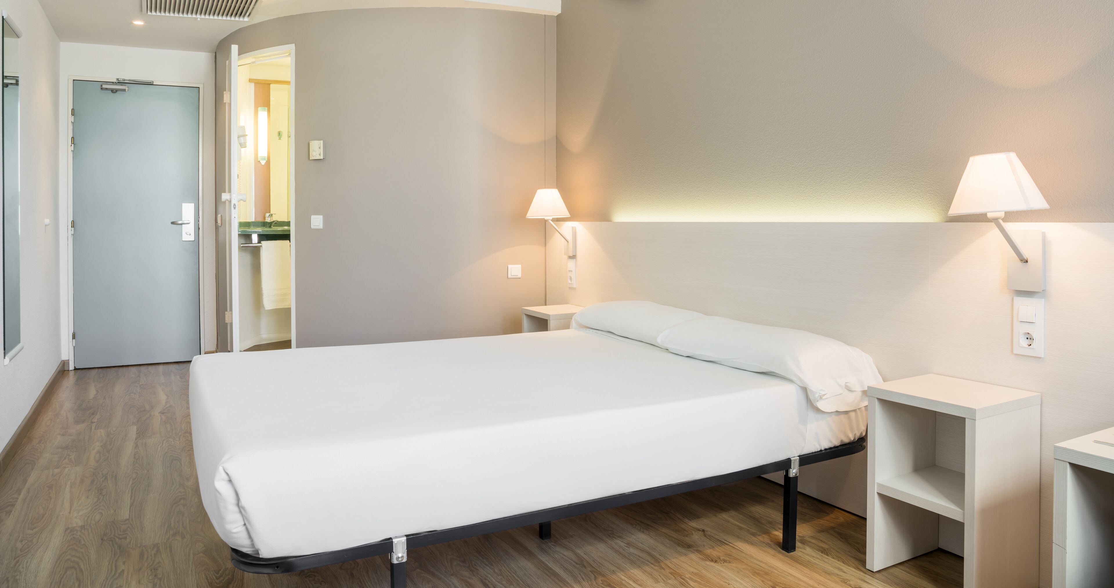 Una habitación de hotel moderna con una cama individual, mesitas de noche y lámparas fijadas a la pared.