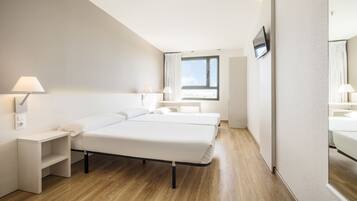 A hotel room with a bed, bedside tables, a TV, and a window.