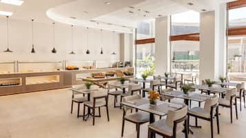 Un comedor moderno con mesas y sillas, un mostrador para buffet, y amplias ventanas.
