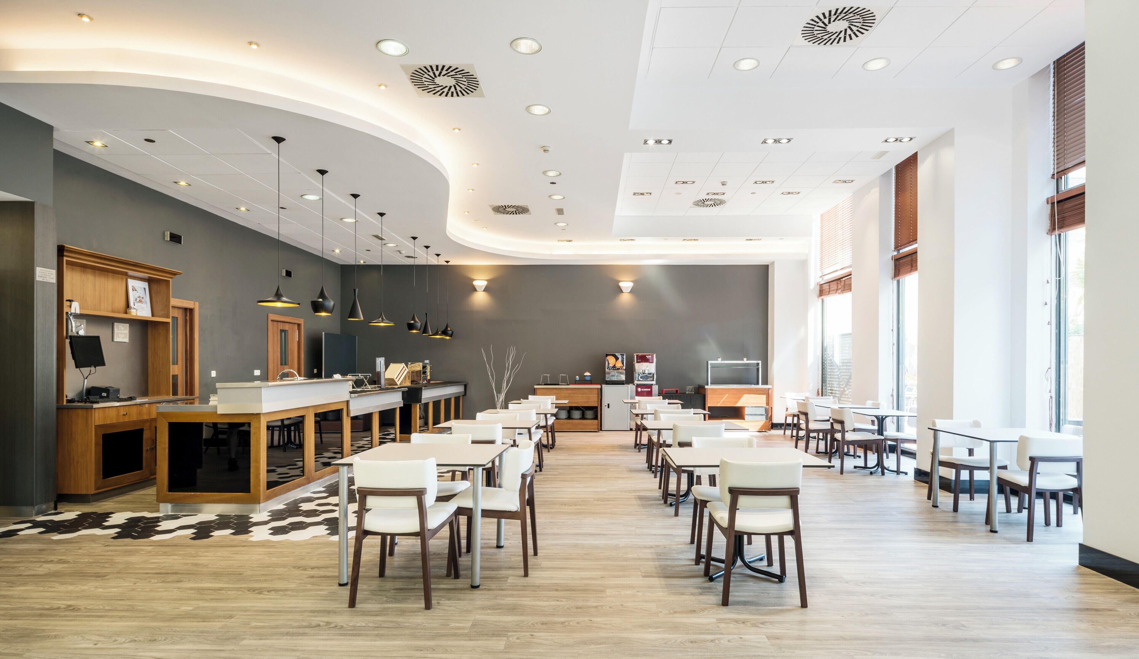 A modern restaurant with a long counter, multiple tables, and a large window.