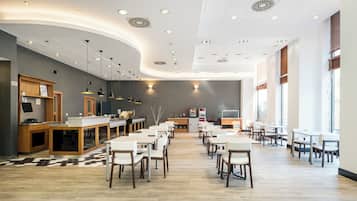 A modern restaurant with a long counter, multiple tables, and a large window.
