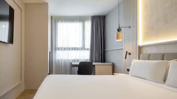 Una habitación de hotel con cama, escritorio, silla y televisor en la pared.