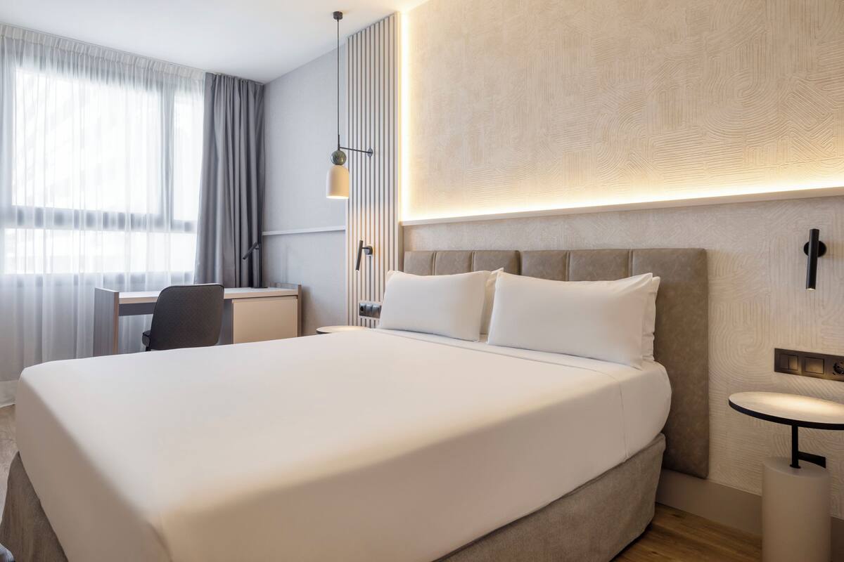 A hotel room with a large bed, a desk, a chair, and a small table.