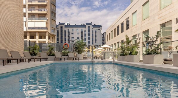 A swimming pool with lounge chairs, a lifebuoy, and potted plants. - Hotel ILUNION Valencia 3 (Valencia)