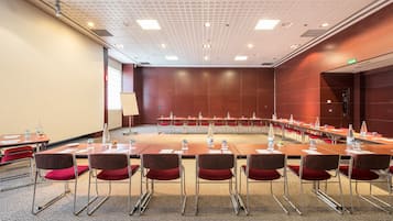 A conference room with a long table, red chairs, and a projector screen.