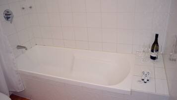 A bathroom with a white bathtub, a toilet, and a shower area.