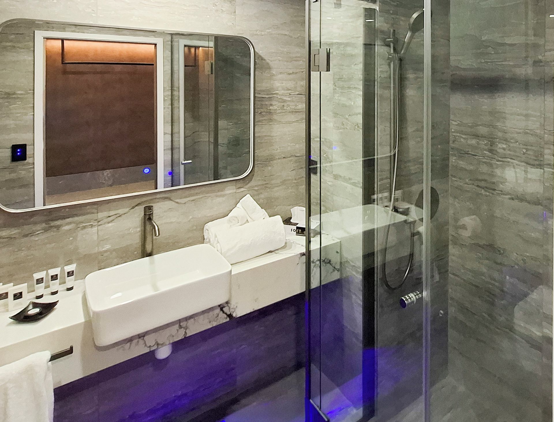 A modern bathroom with a glass shower enclosure, a white sink with toiletries, and a mirror above the sink.