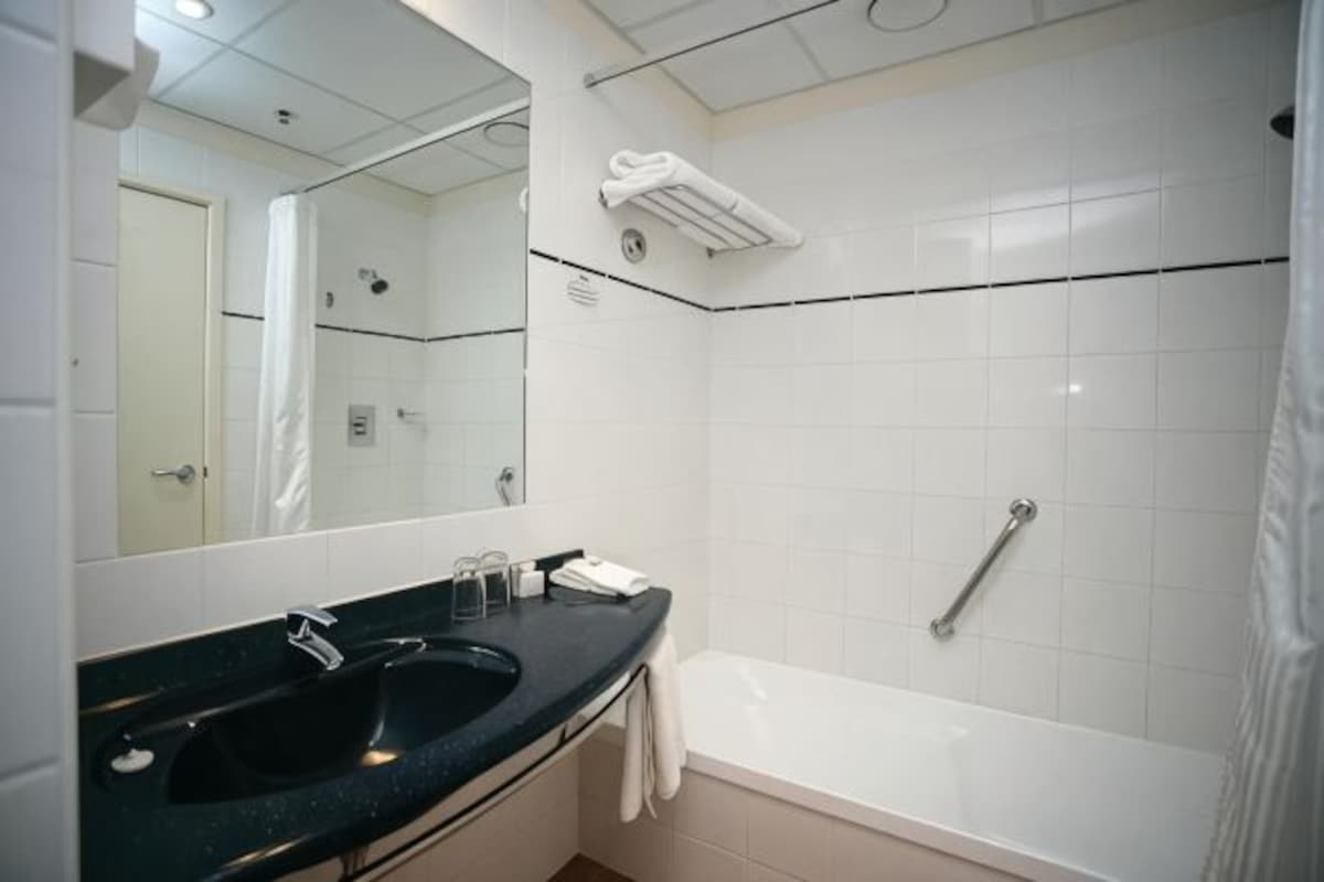 A bathroom with a black sink, a mirror, a white bathtub, and a towel rack.