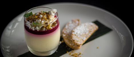 A dessert with a layered appearance, garnished with nuts and a leaf, served on a plate with a piece of bread.