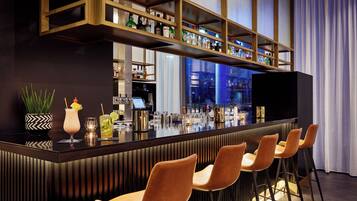 A bar area with a long counter, multiple shelves with bottles, and several bar stools.