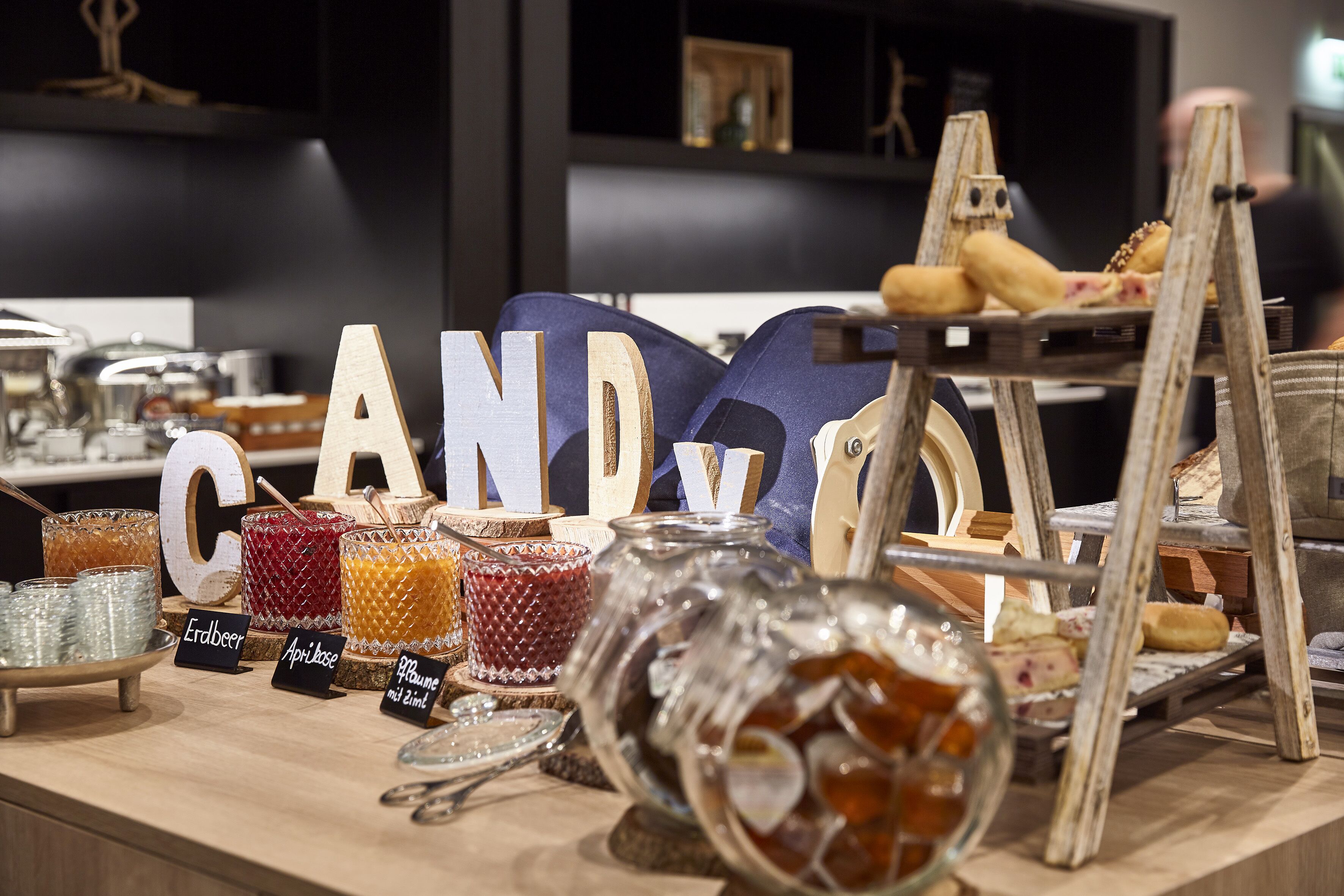 Eine Theke mit verschiedenen Gläsern, beschriftet mit unterschiedlichen Biersorten, Holzbuchstaben die "CANDY COOK" bilden, und einigen Lebensmitteln auf einem Podest.