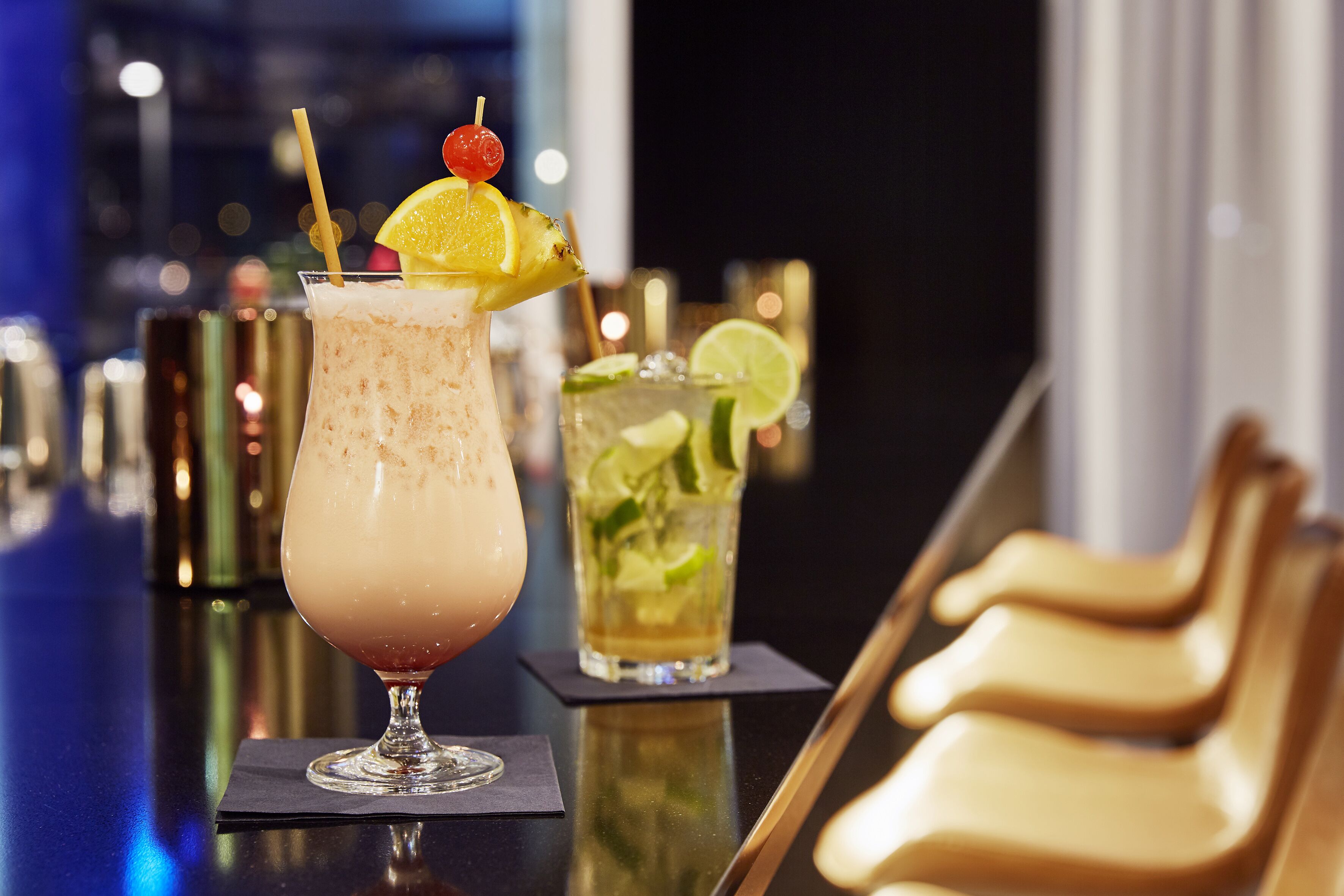 Un coin bar avec deux verres posés sur le comptoir, l’un décoré d’un morceau d’ananas et l’autre de rondelles de citron vert.