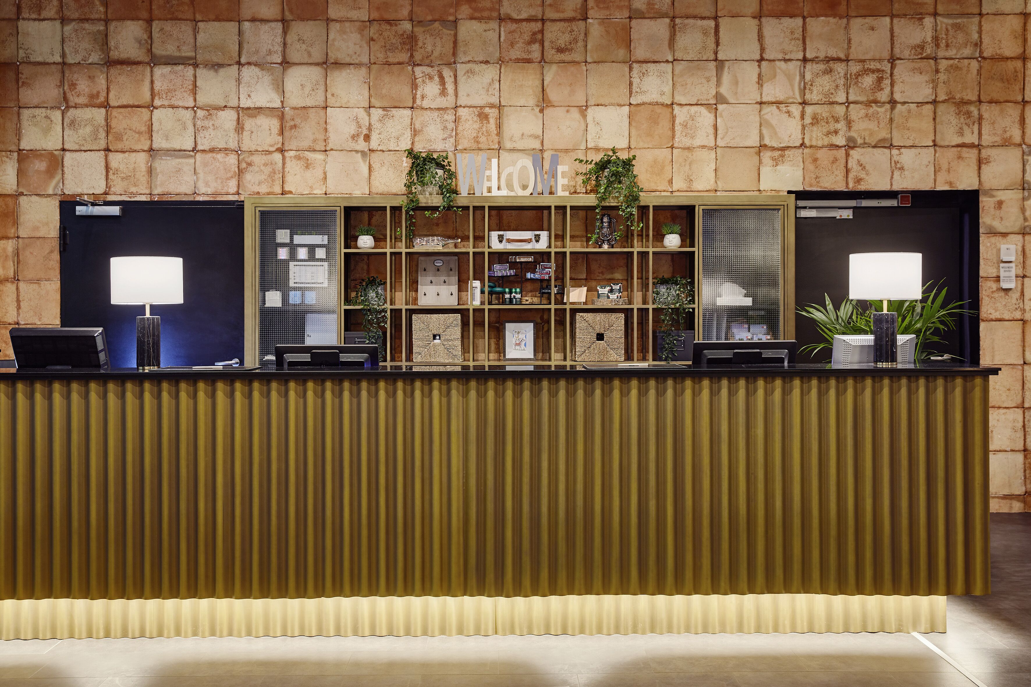 A reception desk with a 'WELCOME' sign, a counter with a computer, and shelves with various items.