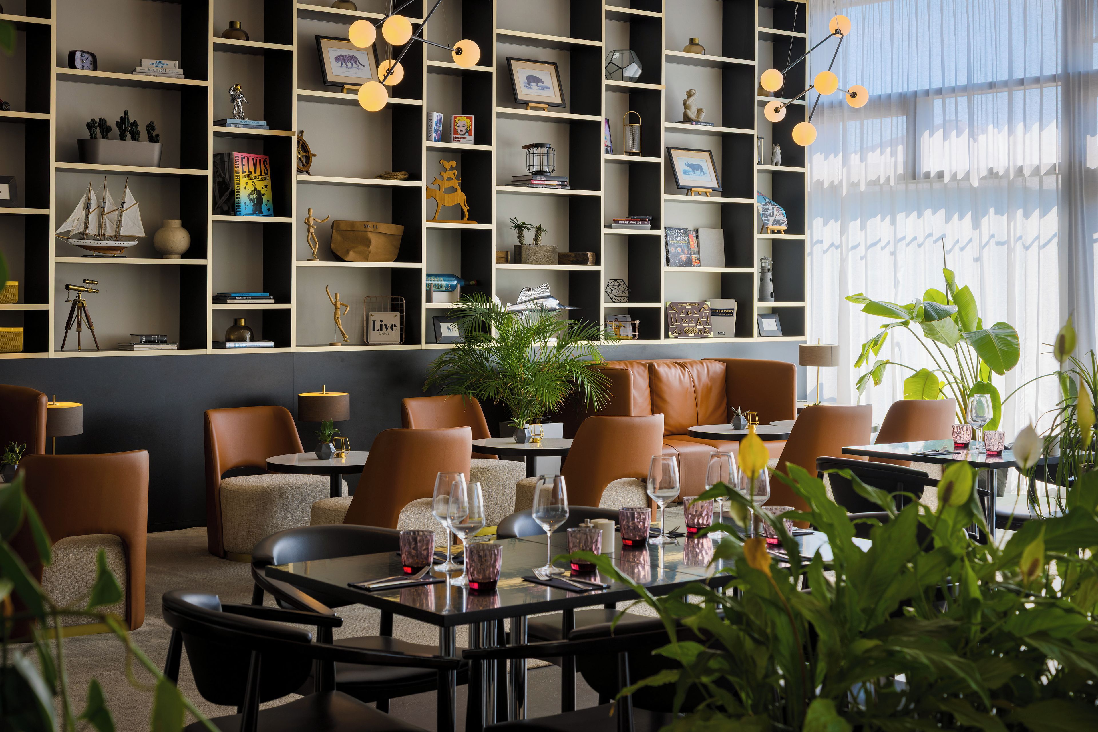 Un interior moderno con zona de comedor, asientos y una estantería llena de objetos varios.