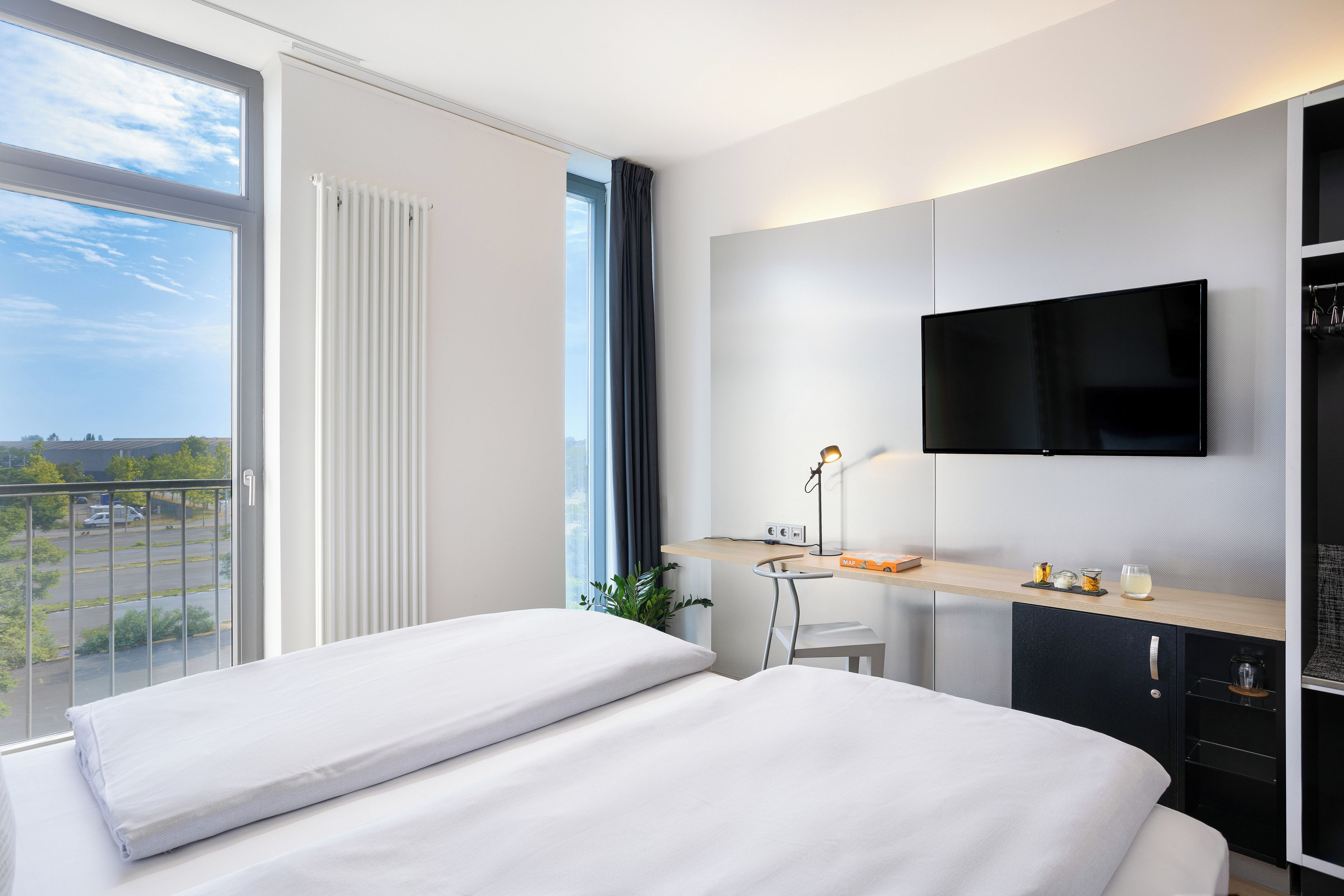 Quarto de hotel moderno com uma cama grande, uma escrivaninha com cadeira, televisão de tela plana na parede e vista para a cidade pela janela.