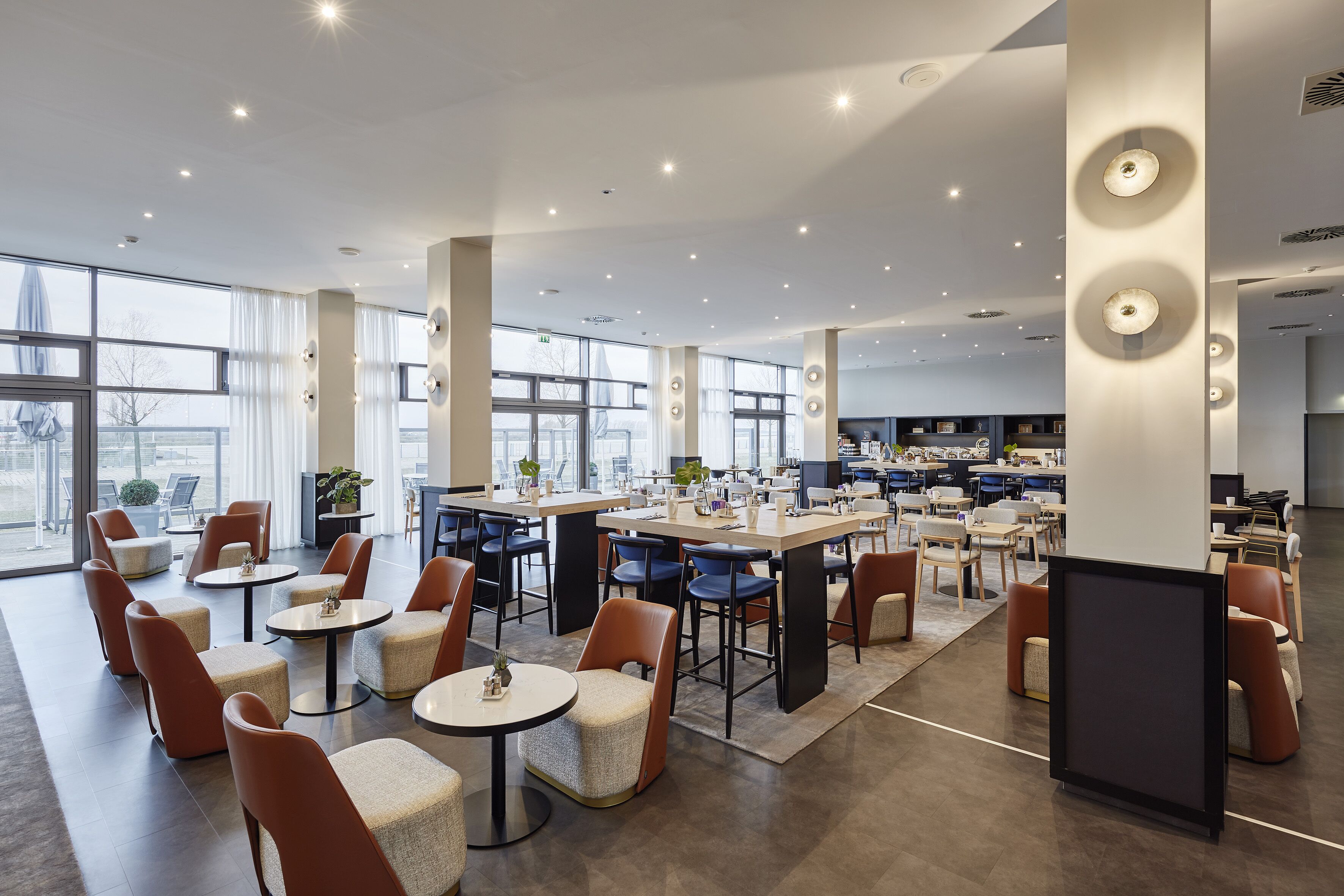 Un comedor amplio y moderno con techos altos, ventanas grandes y una variedad de disposiciones de asientos, incluyendo mesas y sillas.