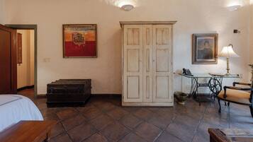 A room with a bed, a desk with a lamp, a wardrobe, and a painting on the wall.