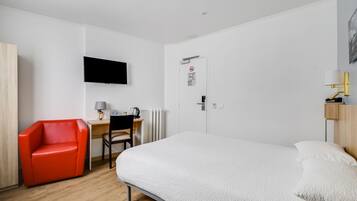 Quarto de hotel com cama, escrivaninha com cadeira, televisão na parede e porta com placa de proibido o acesso.