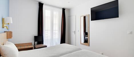 Habitación de hotel con dos camas, un televisor montado en la pared, un escritorio con una silla y una ventana con cortinas.