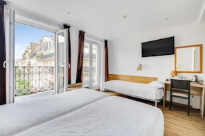 Habitació d'hotel amb dos llits, una taula, una cadira, un televisor i un balcó amb vista a edificis.
