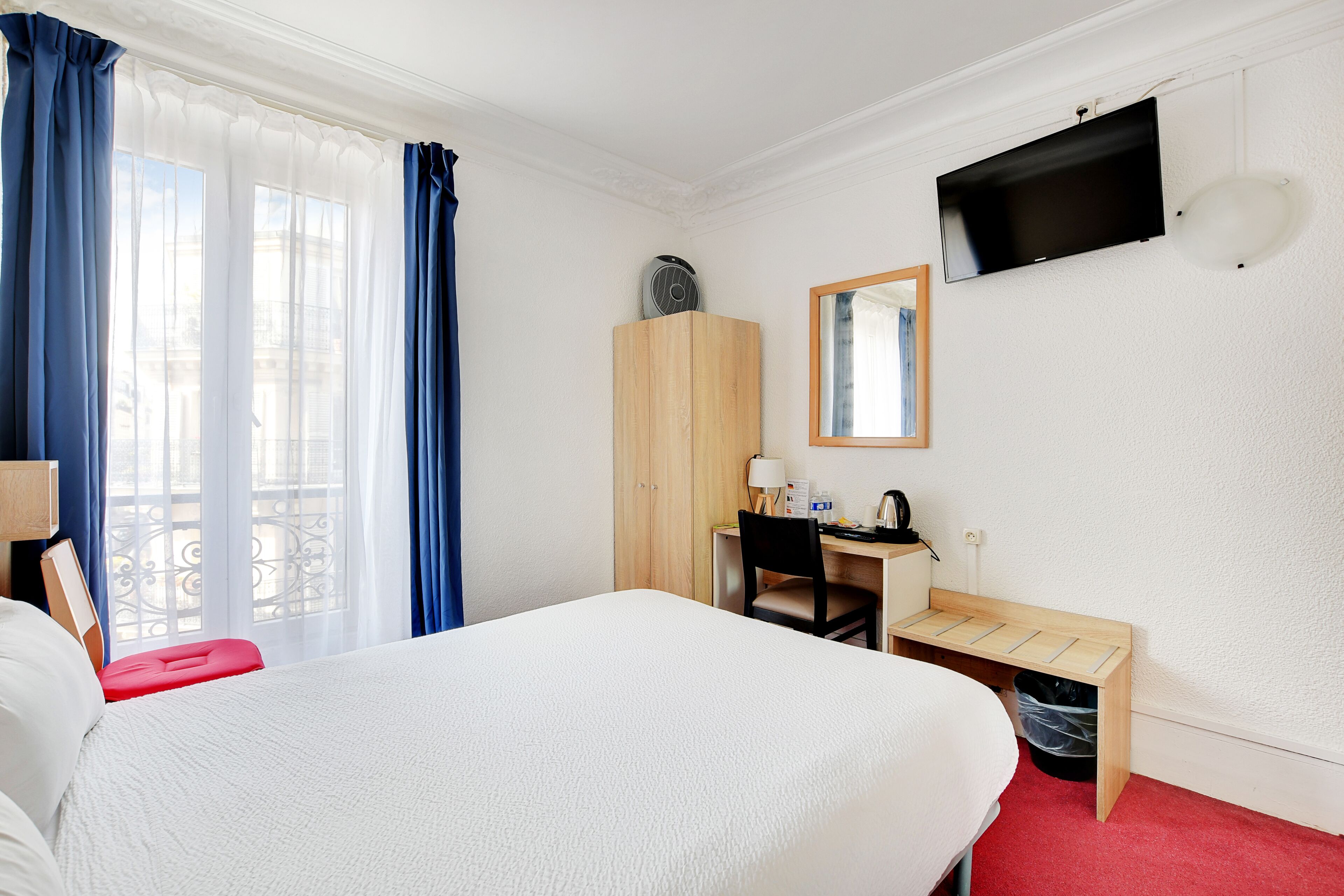 Habitación de hotel con cama, escritorio, silla, televisión y ventana con cortinas.