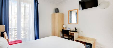 Habitación de hotel con cama, escritorio, silla, televisión y ventana con cortinas.