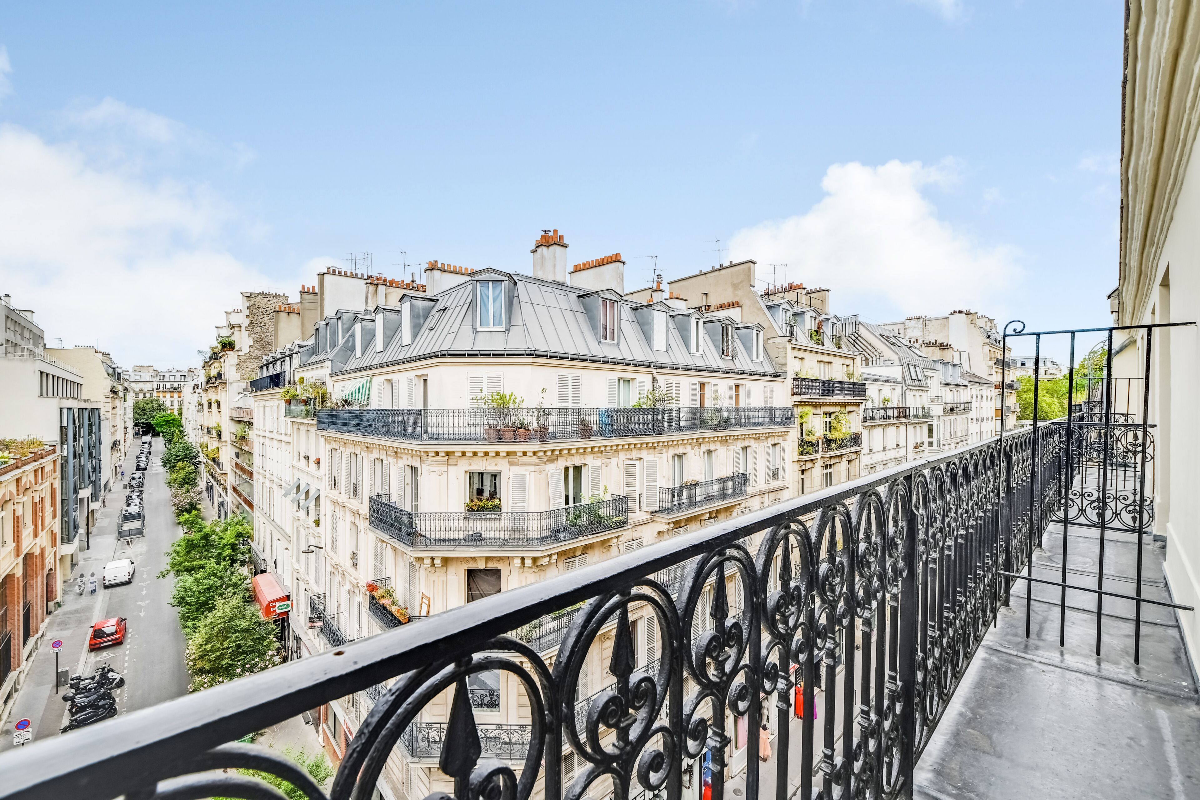 A balcony with wrought iron railings overlooking a street with parked cars and buildings.
