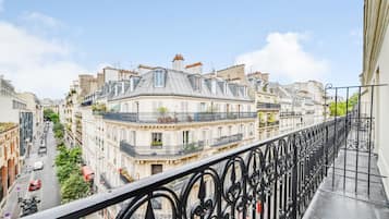 Ein Balkon mit schmiedeeisernen Geländern, der auf eine Straße mit parkenden Autos und Gebäuden blickt.