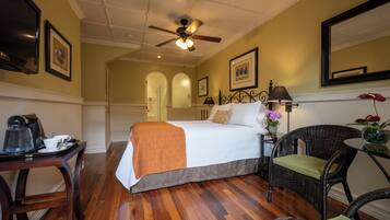 A hotel room with a bed, a desk with a coffee maker, wicker chairs, and a ceiling fan.